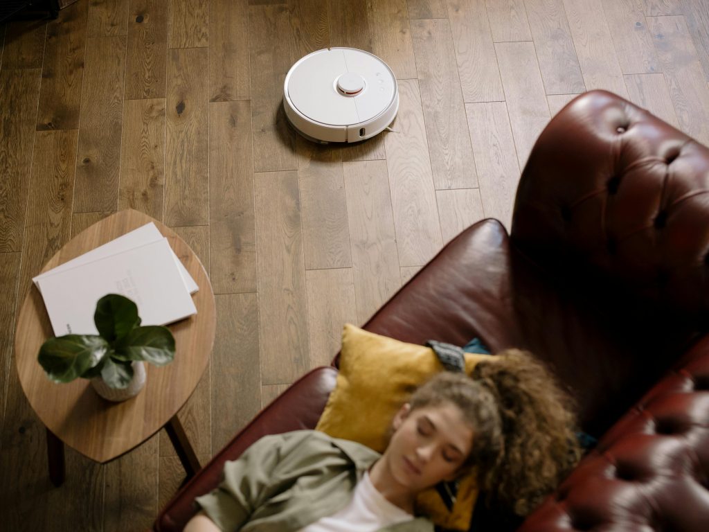 A modern living room with a robotic vacuum and a woman resting, showcasing ease and comfort.